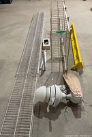 Photo showing two white plastic coated metal racks, yellow painted wood shelf, ceiling fan parts including blades and dome light fixture on concrete floor.