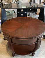 Front view of oval wooden end table with sunburst pattern top, fluted legs, and lower shelf
