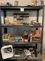 Black metal workshop shelving holding various containers of screws, nailers and small hardware items.