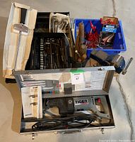 Overview photo showing full lot with Tiger Saw in case, black tool case with socket set, blue bin with clamp ends, vise and tin with rasps.