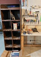 Wood cabinet with ten compartments next to workbench and pegboard with tools.