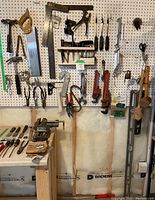 Photo of hand saws, clamps, hand planes, chisels and other hanging workshop tools on pegboard.