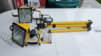 Yellow adjustable tripod work light with foldable legs and dual halogen lamps on a white surface.