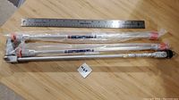 Overview of three airless paint sprayer extension rods next to ruler for scale, showing metal construction and plastic wrap.