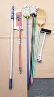All cleaning tools arranged on cardboard including mop bucket frame, extension rod, mops, broom, brush and scraper.