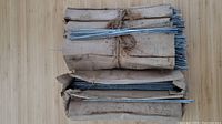Two bundles of straight metal wires wrapped in brown paper, tied with string, laying on a wooden surface.