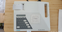 Front view of the Siemens Burdick EK10 EKG machine with keypad, screen, and attached paper roll for printout.