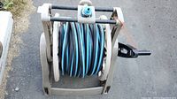 Full view of garden hose coiled on beige plastic hose reel showing black winding handle and blue-black hose color