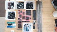 Top-down view showing multiple white trays of various black IC sockets of differing pin counts, foam inserts with socket strips, and several long socket strips along right edge of table.
