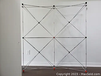 Fully expanded Nomadic Instand display stand pop-up frame showing grid structure with metal rods and red and black connectors.