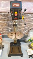 Full front view of drill press on workbench showing base, column, table and head.