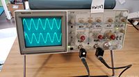Front left view of Tektronix 2235 oscilloscope showing two waveform signals on screen and two black probes connected.
