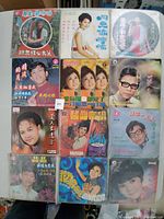 Set of 12 Chinese 45RPM vinyl records in plastic sleeves with various male and female singers on the cover.