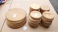 Multiple stacks of wooden round bases on cardboard, clearly showing both large 10.5 inch bases and smaller 5 inch bases labeled with handwritten sticky notes.