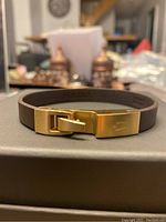 Close-up photo of brown leather strap bracelet with gold-tone clasp showing Bulova logo