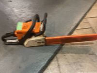 Side view of an orange Stihl chainsaw with orange protective bar cover on the blade.