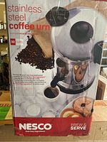 Photo of the front of the box showing the Nesco stainless steel coffee urn, capacity of 30 cups, and an image of the urn with a coffee cup and food items around it.