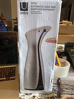 Box showing front view of Umbra Otto automatic soap and sanitizer dispenser with brand, capacity and designer info.