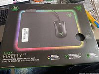 Front view of the Razer Firefly V2 Gaming Mousepad box highlighting customizable Chroma RGB lighting and hard surface features.