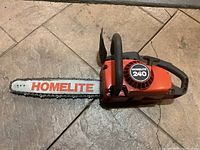 Full side view of Homelite 240 chainsaw showing orange and black body, metal bar with chain and Homelite logo on the bar.