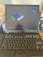 Front view of IBM Lenovo ThinkPad laptop powered on displaying the IBM ThinkPad startup screen with Centrino and Intel technology logos. Keyboard and TrackPoint visible.