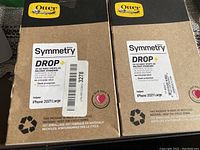 Photo showing front of two OtterBox Symmetry Series Drop+ case boxes for iPhone 11 2021 Large, with branding and key features visible.