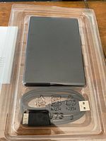 External hard drive and USB cable packaged in transparent plastic tray.