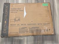 Boxed Delta Children toddler bed showing front with model number and safety warnings.