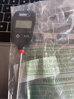 Weber instant read thermometer in plastic packaging showing front with digital display and buttons