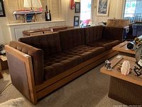 Front right angle view showing tufted seat and back cushions, wooden frame and overall style