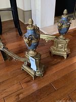 Front view of both andirons on hardwood floor showing urn shape and decorative mounts