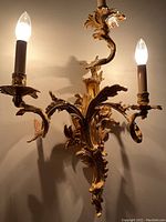 Full front view of gilt brass wall sconce with three lit candle-style bulbs