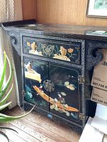 Front view of cabinet showing carved relief appliqués of figures in a boat, lotus and bamboo scene, metal latch hardware.