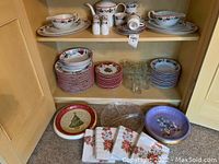Cabinet top shelf showing gravy boats, sugar bowl, creamer, salt & pepper shakers; middle shelf full stacks of plates and glass tumblers; bottom shelf decorative items