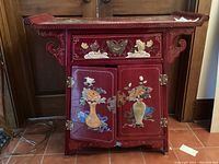 Front view of red lacquer altar cabinet showing drawer, double doors, brass hardware, and inlaid floral vases.