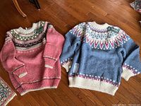 Overview of two ladies XL hand-knit wool Fair Isle sweaters laid flat on wood floor