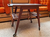 Side view of the teak bar cart showing removable top tray and lower lattice shelf with casters