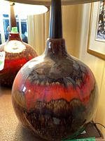 Close-up of one lamp’s ceramic base showing red, brown and cream drip glaze finish