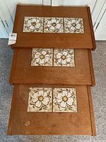 Three teak nesting tables stacked, tops feature ceramic tiles with white daisy designs