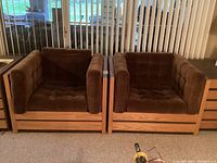 Front view of two identical cube-shaped chairs with solid wood bases and tufted brown corduroy cushions side by side