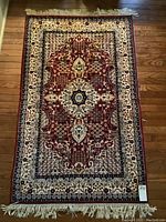 Full view of rectangular rug laid flat on hardwood floor showing overall medallion design and fringed ends