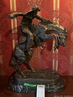 Full front view of bronze cowboy on rearing horse atop marble base