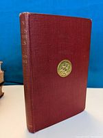 Front and side view of the 1937 Rudyard Kipling book 'Plain Tales From the Hills' showing burgundy cloth cover and gold embossed details