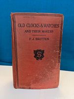 Front cover of hardcover book 'Old Clocks and Watches and Their Makers' by F. J. Britten in red cloth with black text and emblem
