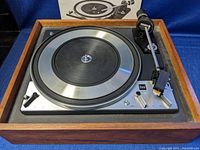 Front wide shot of Dual 1218 turntable with wooden case, metal platter, tonearm, and part of the manual in the background.