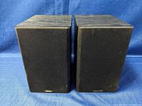 Front view of pair of Energy bookshelf speakers with black grille cloth, one badge missing on the right speaker