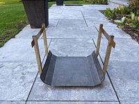 Front angle view of the firewood holder showing the steel base tray with upward curved edges and brass vertical and horizontal supports.