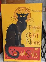 Photo of the front of the large poster showing a black cat with yellow eyes and French text on a yellow and red background.