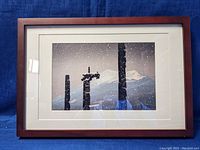 Framed Japanese art print showing snowy landscape with wooden poles and mountain background, on blue cloth background.
