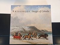 Front cover of a large hardcover art book titled 'Krieghoff Images of Canada' by Dennis Reid showing a winter horse-drawn sleigh scene.